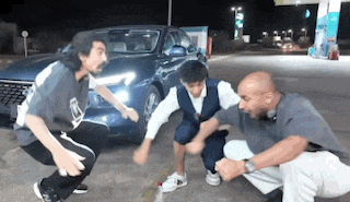 a group of people are squatting in front of a car at a gas station .