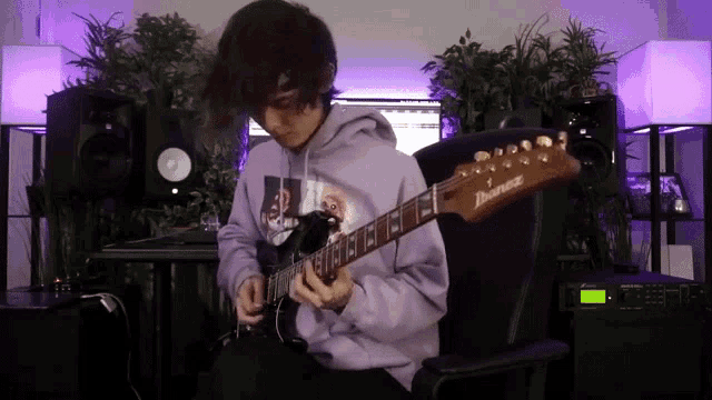 a man in a purple hoodie is playing an ibanez electric guitar