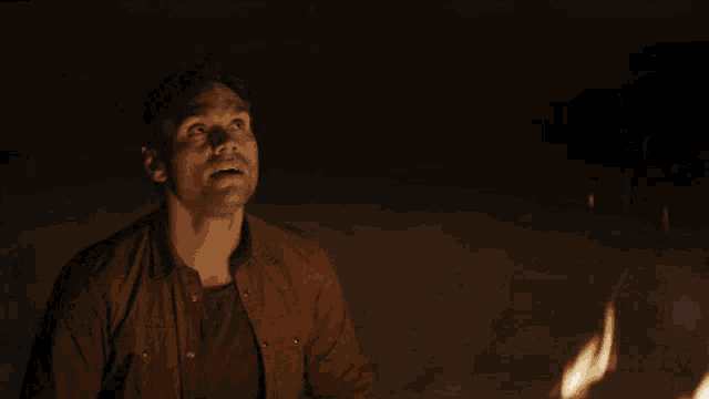 a man sitting in front of a fire looking up at the sky