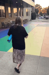 a woman in a black shirt is walking down a sidewalk holding a blue bag