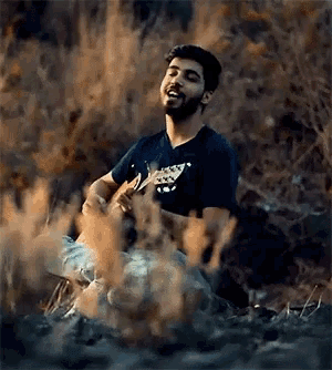 a man with a beard is playing a guitar in the woods
