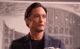 a man in a suit is holding a cup of coffee in front of a picture of a colosseum .