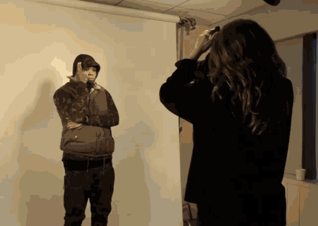 a woman taking a picture of a man in a hooded vest