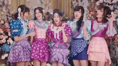 a group of girls in purple and pink dresses are standing next to each other in front of flowers .