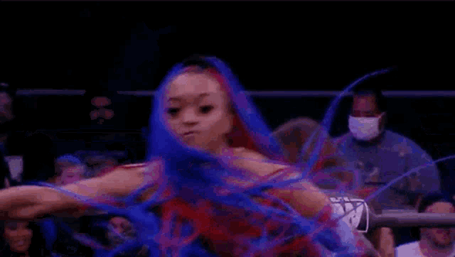 a woman with blue and red hair is dancing in a wrestling ring .