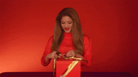 a woman in a red sweater is opening a red box with a gold ribbon