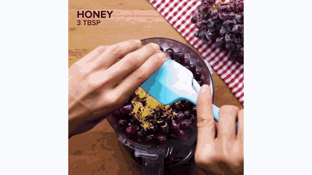 a person is adding honey to a bowl of grapes with a spoon .