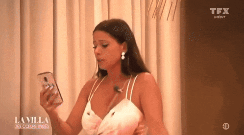 a woman in a white dress is holding a cell phone in her hand .