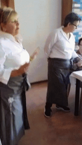 a woman in a white shirt is standing next to another woman in a black apron