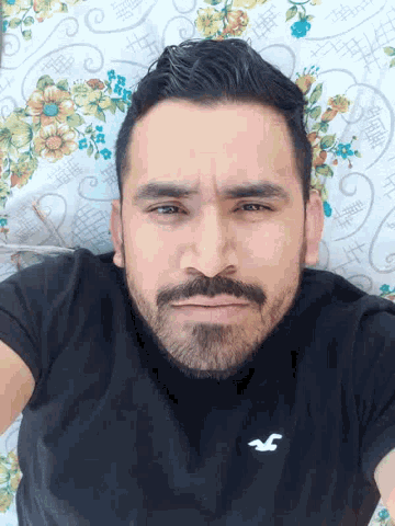 a man with a beard is laying on a bed with a black shirt that has the letter s on it