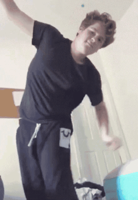 a man in a black shirt and black sweatpants is dancing in a room