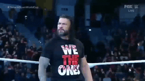 roman reigns is walking out of a wrestling ring wearing a we the ones shirt .