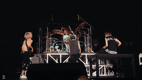 a band on stage with a drummer wearing a black shirt that says ' i 'm a king ' on it