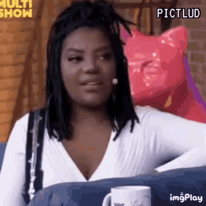 a woman with dreadlocks is sitting on a couch with a pink cat in the background .