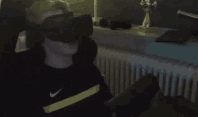 a man wearing a virtual reality headset is sitting in a chair in a dark room .