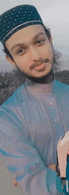 a young man wearing a blue shirt and a black hat is standing with his arms crossed .