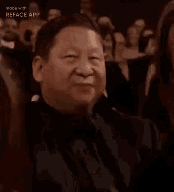a man in a black suit and bow tie is sitting in a crowd of people applauding .
