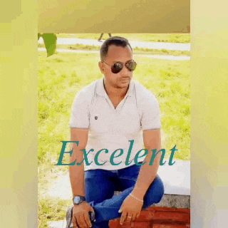 a man wearing sunglasses and a white shirt is sitting on a brick wall in a park .