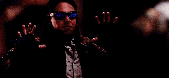 a man wearing sunglasses and a suit is holding a blue object in his hands .