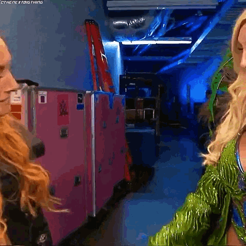 two women are standing next to each other in a hallway and one of them is wearing a green outfit .