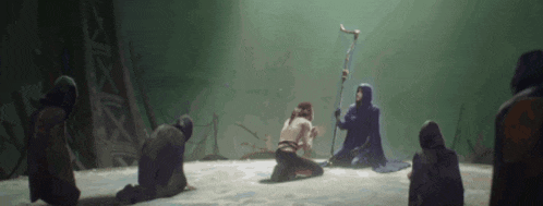a group of people are kneeling down in a dark room with a man holding a staff .
