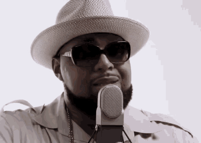a man wearing a hat and sunglasses holds a microphone