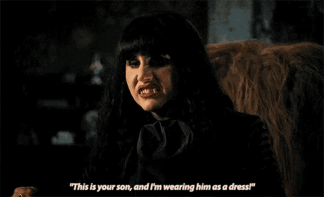 a woman in a black dress is sitting in a chair and talking to a man in a dress .