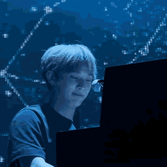 a man in a blue shirt is playing a keyboard in a dark room
