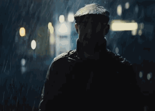 a man wearing a hat and glasses stands in the rain