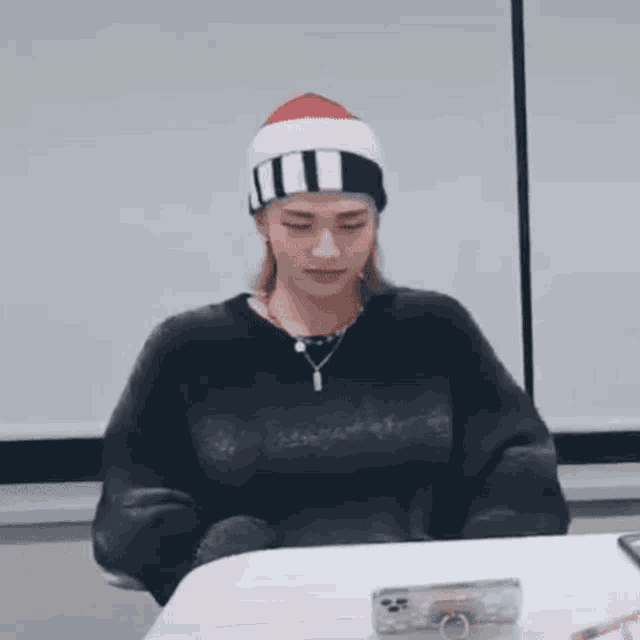 a person wearing a beanie and a sweater is sitting at a table .