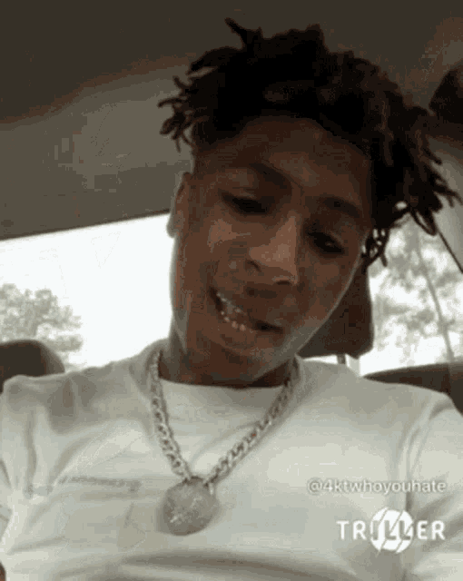 a young man with dreadlocks is sitting in a car wearing a white shirt and a necklace .
