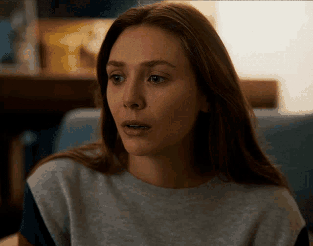 a woman with long brown hair is wearing a grey sweater