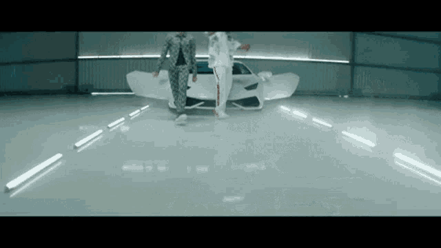 two men are standing in front of a white car in a warehouse .