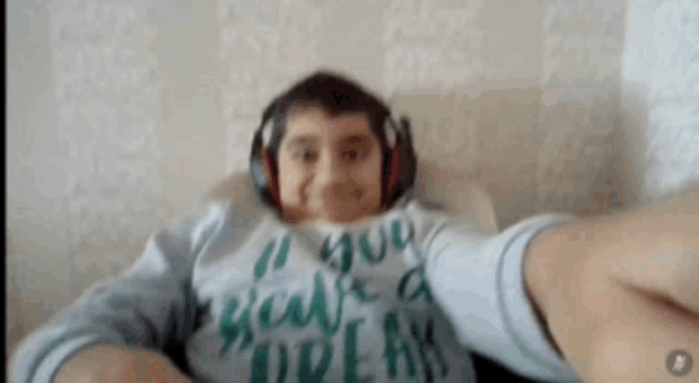 a young boy wearing headphones and a shirt that says " i believe a dream " is taking a selfie .