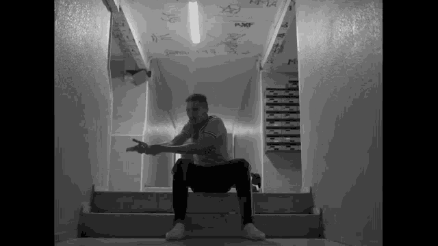 a black and white photo of a man sitting on a set of stairs with a shirt that says fly emirates