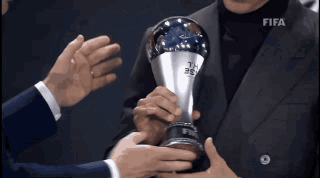 a man in a suit holding a trophy that says fifa