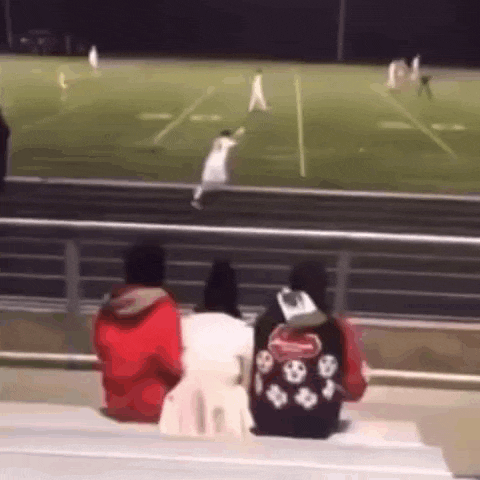 a group of people are sitting on a bench watching a soccer game .
