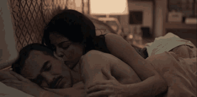 a man and a woman are laying in bed and the woman is kissing the man 's neck