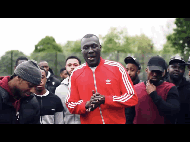 a man in a red adidas jacket stands in a crowd of men