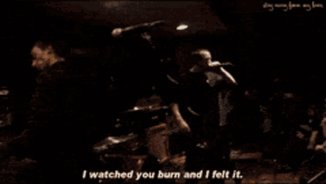 a man singing into a microphone in front of a crowd with the words " i watched you burn and i felt it "