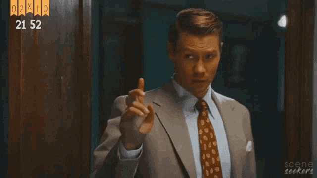 a man in a suit and tie pointing at the camera with the number 21 52 above him