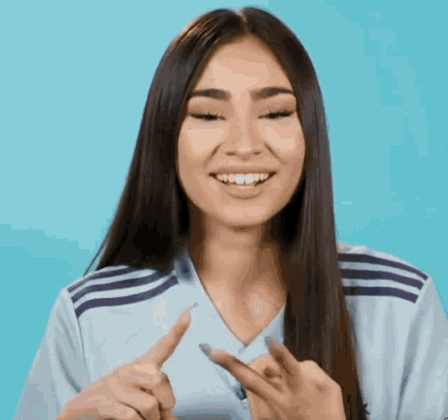 a woman with long hair is wearing a blue adidas shirt and smiling