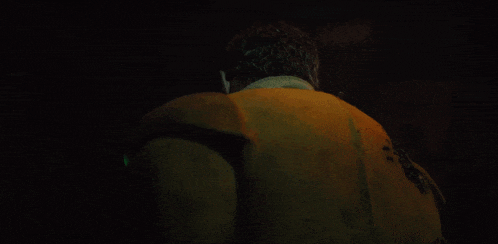 a man in a yellow jacket is standing in the dark with a green light behind him