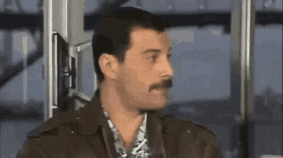 a man with a mustache is sitting in front of a window and looking at the camera .