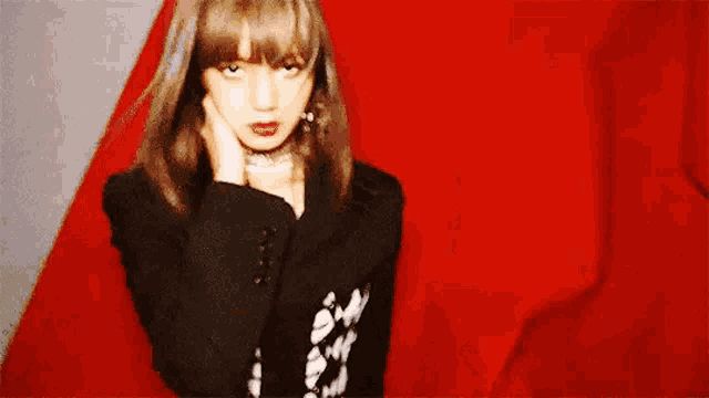 a woman in a black jacket and choker is standing in front of a red background .