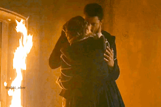 a man and woman hugging in front of a fire