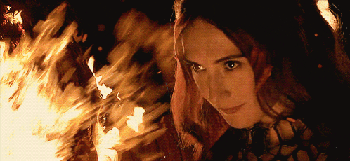 a woman with red hair is standing in front of a large fire