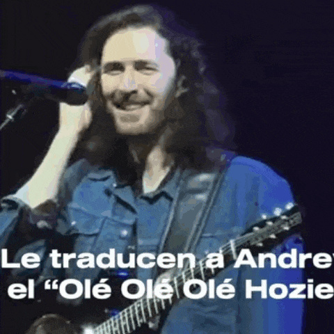 a man with long hair is singing into a microphone while playing a guitar .