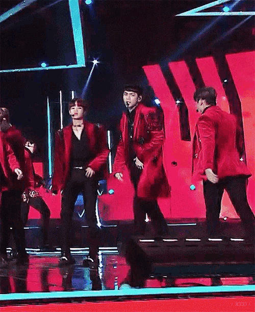 a group of men are dancing on a stage while wearing red jackets .