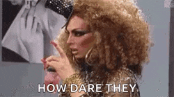 a drag queen with a big hairdo is pointing at something and saying `` how dare they '' .